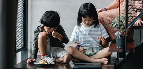 亚洲儿童在平板电脑上观看视频和在家吃小吃 · 免费素材图片