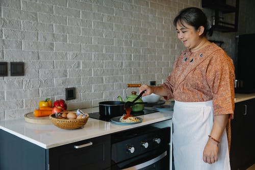 性格开朗的高级民族家庭主妇在厨房里菜时倒在面食上 · 免费素材图片