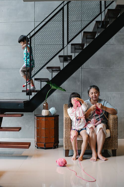 亚洲孩子下楼在别墅里，而姐姐和祖母坐在扶手椅上，编织 · 免费素材图片