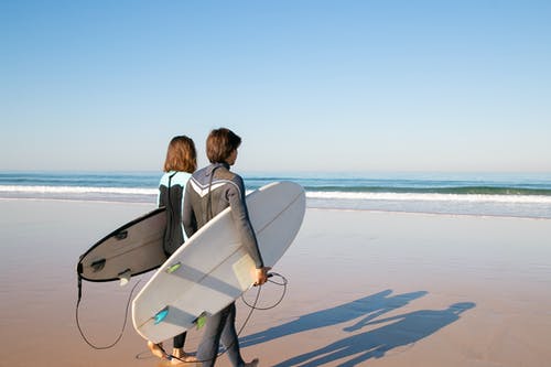 黑夹克携带白色冲浪板在海滩上的女人 · 免费素材图片