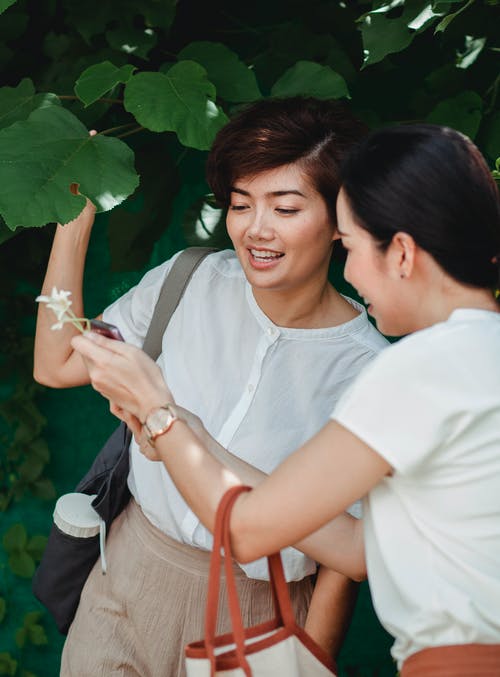 无法识别女人显示智能手机到树附近微笑亚洲女友 · 免费素材图片