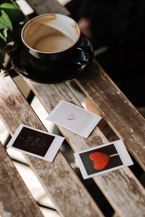 棕色木制的桌子上的黑色陶瓷杯旁边的白色和红色的花卡 · 免费素材图片