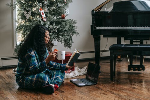 在膝上型计算机和圣诞树附近的黑人妇女阅读书 · 免费素材图片