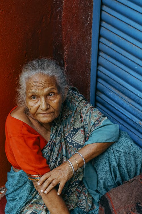 坐在墙壁附近的老年种族妇女 · 免费素材图片