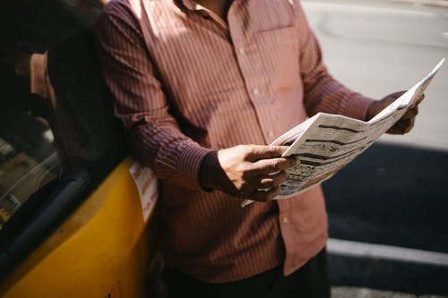 在镇上作物族裔男性出租车司机阅读报纸 · 免费素材图片