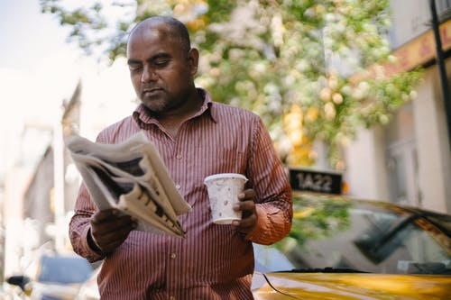 严重的民族出租车司机与外卖咖啡和报纸 · 免费素材图片