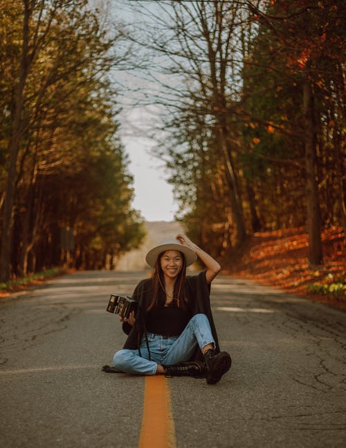 快乐的亚裔女子和照相机一起坐乡下路 · 免费素材图片