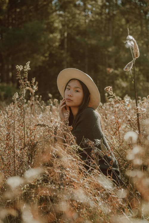 迷人的亚裔女子，在长满草的草地上休息的帽子 · 免费素材图片