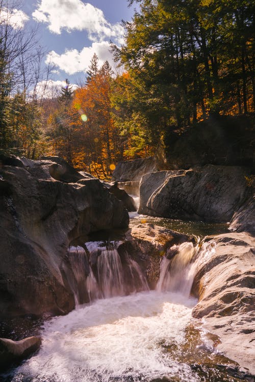 在秋天的树林大石头之间流动的瀑布 · 免费素材图片