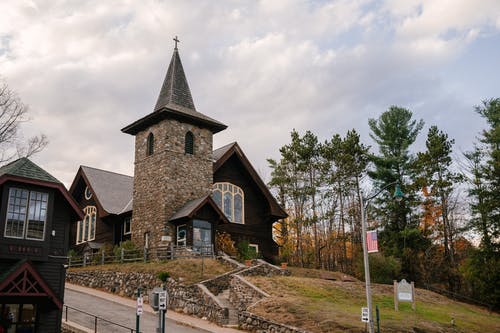 古老的教堂门面位于秋天森林附近的丘陵地形对多云的天空 · 免费素材图片