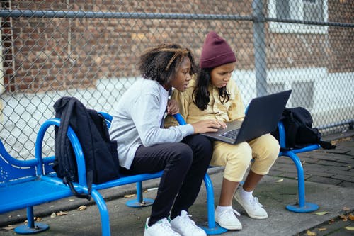 细心的多种族女学生在街头的长椅上看笔记本电脑 · 免费素材图片