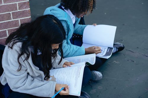 聪明的多民族女孩在教科书中写作和做作业 · 免费素材图片