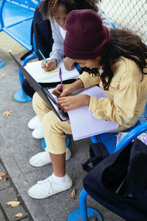 作物与抄写本和笔记本电脑在大街上学习的多民族小学生 · 免费素材图片