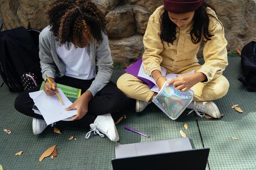 作物在笔记本电脑附近人行道上做作业的不同学童 · 免费素材图片