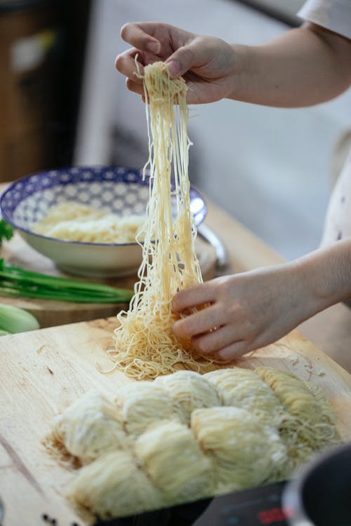 持有黄色面食棕色木制的桌子上的人 · 免费素材图片