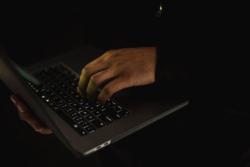 作物在黑暗中在笔记本电脑键盘上打字的不露面男人 · 免费素材图片