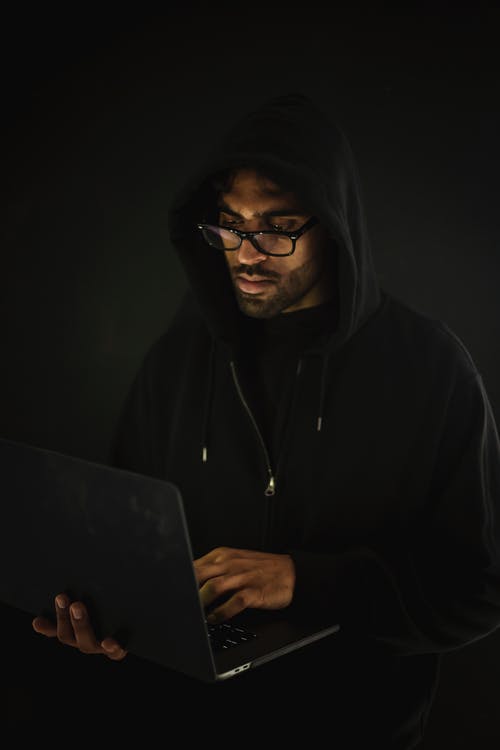 帽衫的体贴的人在暗室使用膝上型计算机 · 免费素材图片