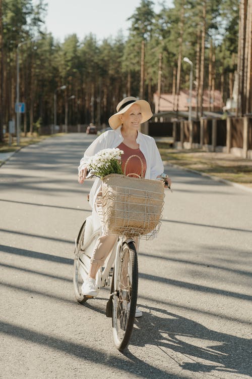 白色长袖衬衫和棕色的帽子，骑着黑色自行车在路上的女人 · 免费素材图片