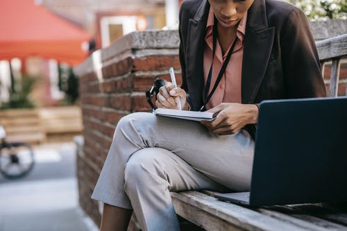 黑色西装外套和灰色裤子，坐在棕色的木凳上看书的女人 · 免费素材图片