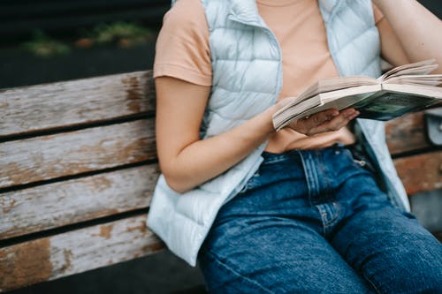 白衬衫和蓝色牛仔牛仔裤，坐在棕色的木凳上看书的女人 · 免费素材图片