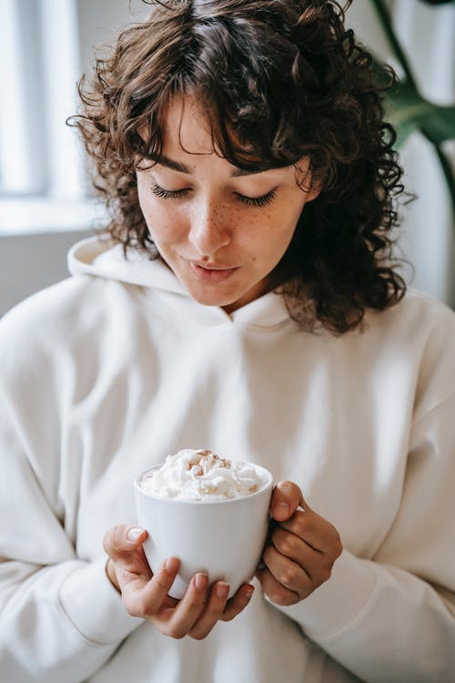 拿着白色陶瓷杯子与白色奶油的白色长袖衬衫的女人 · 免费素材图片