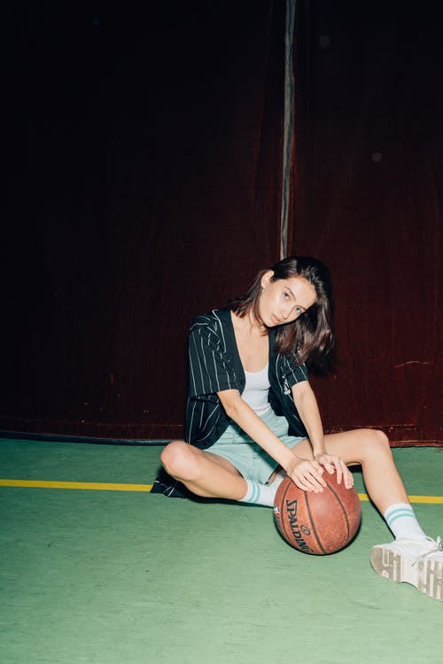 黑色和白色衬衫和黑色短裤坐在篮球上的女人 · 免费素材图片