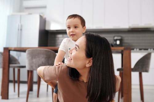 女人抱着一个坐在她身后的男孩 · 免费素材图片