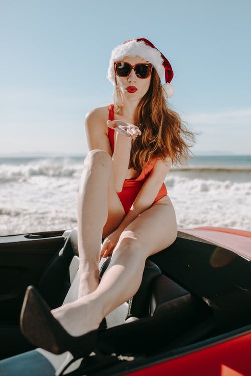红色比基尼泳装的妇女与圣诞老人帽子坐一辆敞篷车汽车 · 免费素材图片