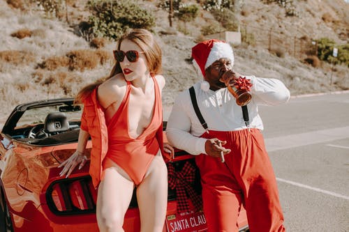 圣诞老人衣服的男人喝酒和吸烟与一个性感的女人 · 免费素材图片