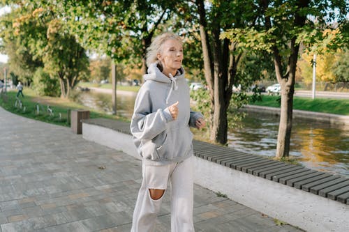 穿着灰色外套站在水附近的灰色混凝土路面上的女人 · 免费素材图片