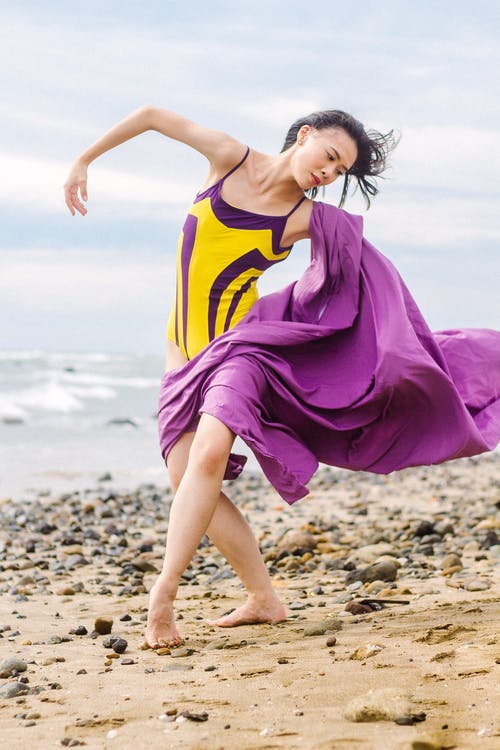 紫色和黄色的意大利面条皮带站在海滩上的女人 · 免费素材图片