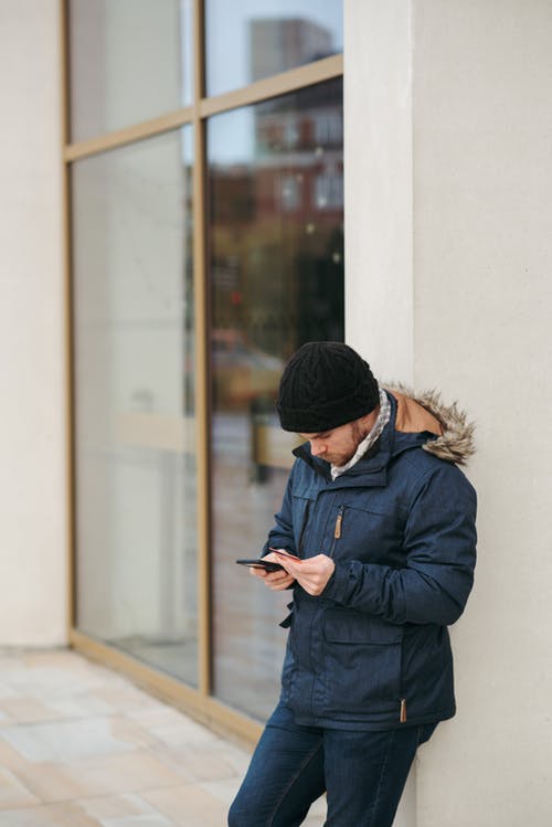 黑色编织帽和黑色外套使用智能手机的人 · 免费素材图片