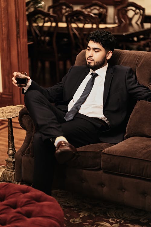 黑色西装的男人坐在棕色的沙发椅子上，拿着玻璃杯 · 免费素材图片