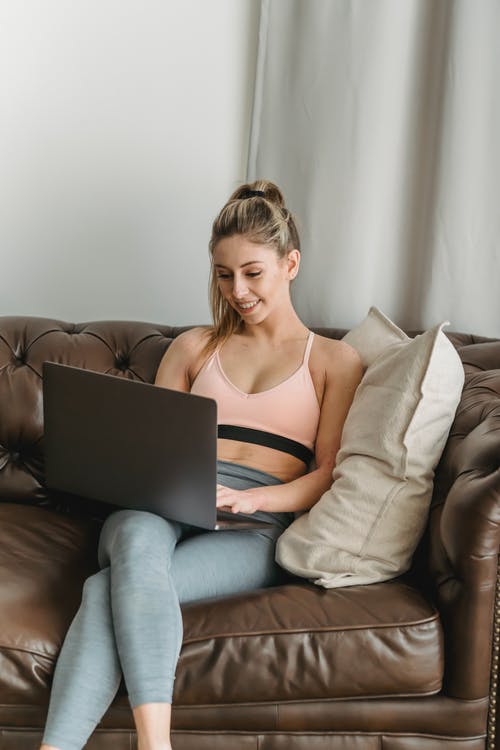 黑色背心坐在沙发上使用macbook的女人 · 免费素材图片