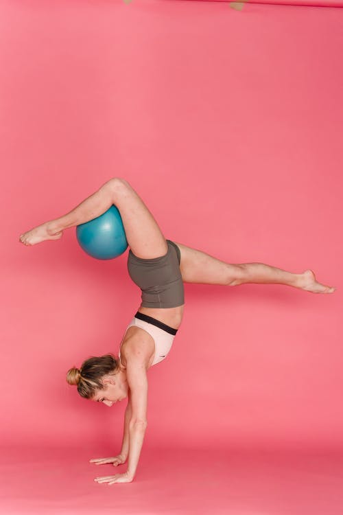黑色运动胸罩和黑色短裤的女人在粉红色的瑜伽垫上弯曲她的身体 · 免费素材图片
