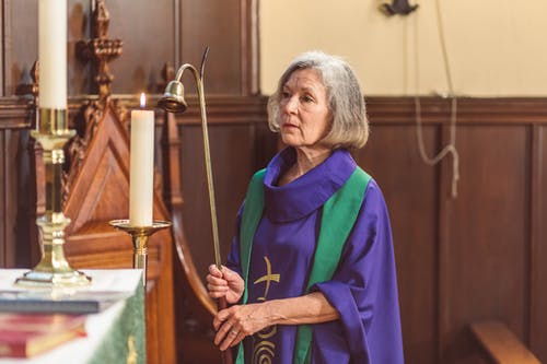 穿着紫色 Chasuble 的女人拿着蜡烛吸管 · 免费素材图片