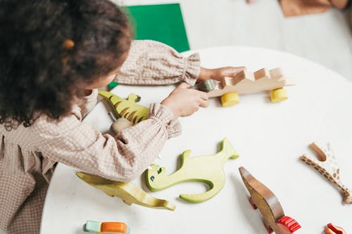 年轻女孩玩白色桌上的木制玩具的开销照片 · 免费素材图片
