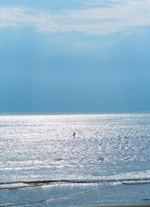 不可识别的运动员，在闪亮的波浪海洋，在蓝蓝的天空下 · 免费素材图片