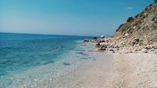 白天蓝色海滩附近的灰色岩层 · 免费素材图片