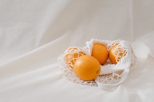 在白色纺织品上的四个橙色水果 · 免费素材图片