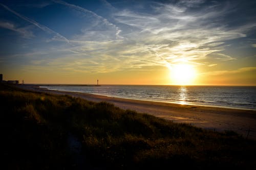 日落期间水体旁边的海岸 · 免费素材图片