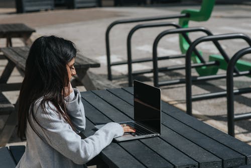 笔记本电脑在街边桌上工作的族裔女商人 · 免费素材图片