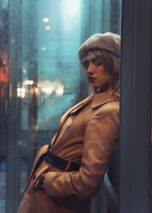 站在玻璃窗口旁边的棕色外套的女人 · 免费素材图片