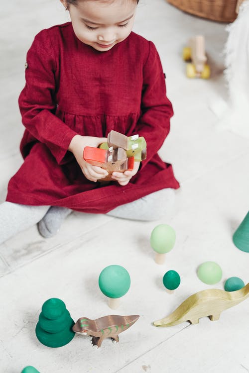 红色长袖连衣裙坐在白色的地上玩玩具的女孩 · 免费素材图片