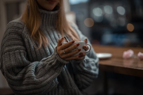 拿着白色陶瓷杯子的灰色针织毛衣的女人 · 免费素材图片