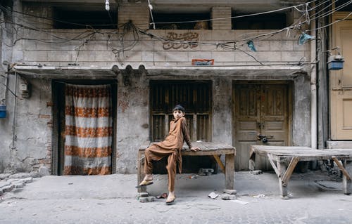 一个穿着棕色shalwar Kameez的男孩坐在木桌上 · 免费素材图片