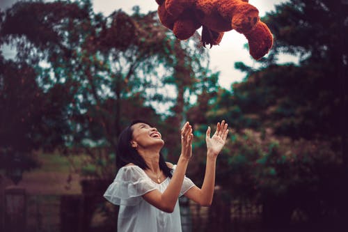 白色连衣裙和棕色的玩具熊一起玩的女人 · 免费素材图片