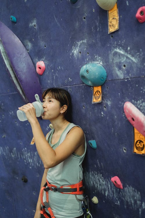 亚洲女登山者饮用水附近攀岩墙 · 免费素材图片