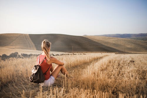 红色背心和白色短裤，背着背包坐在棕色草地上的女人 · 免费素材图片