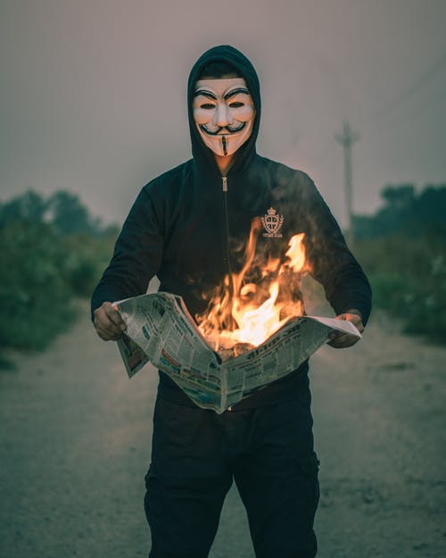 戴着盖伊·福克斯面具的人拿着燃烧的报纸 · 免费素材图片